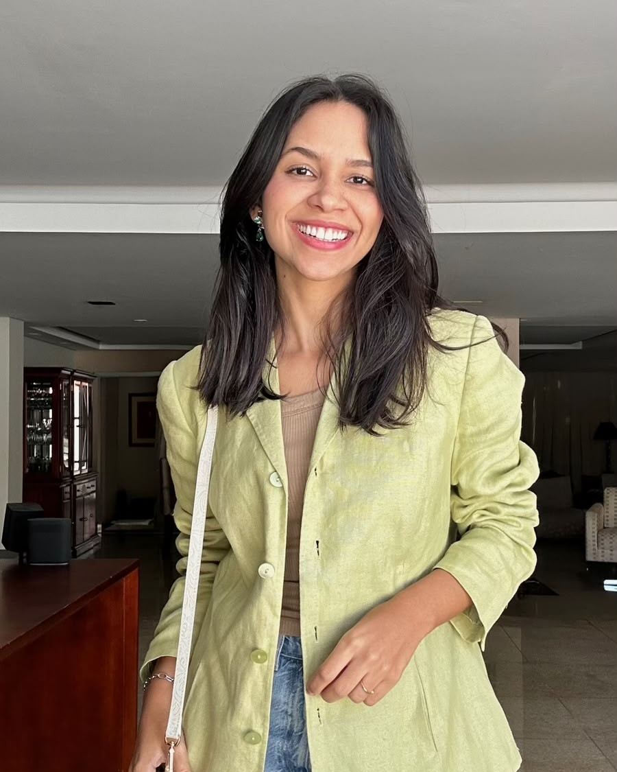 Gesiene Maise sorrindo, vestindo blazer de linho verde e calça jeans